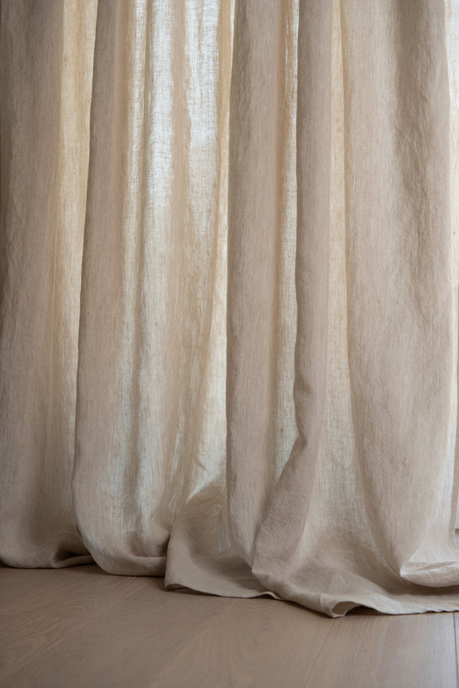 Semitransparent beige linen curtain, naturally falling on wooden floor - discover the allure of breeze oatmeal linen curtain draping gracefully on a wooden surface.