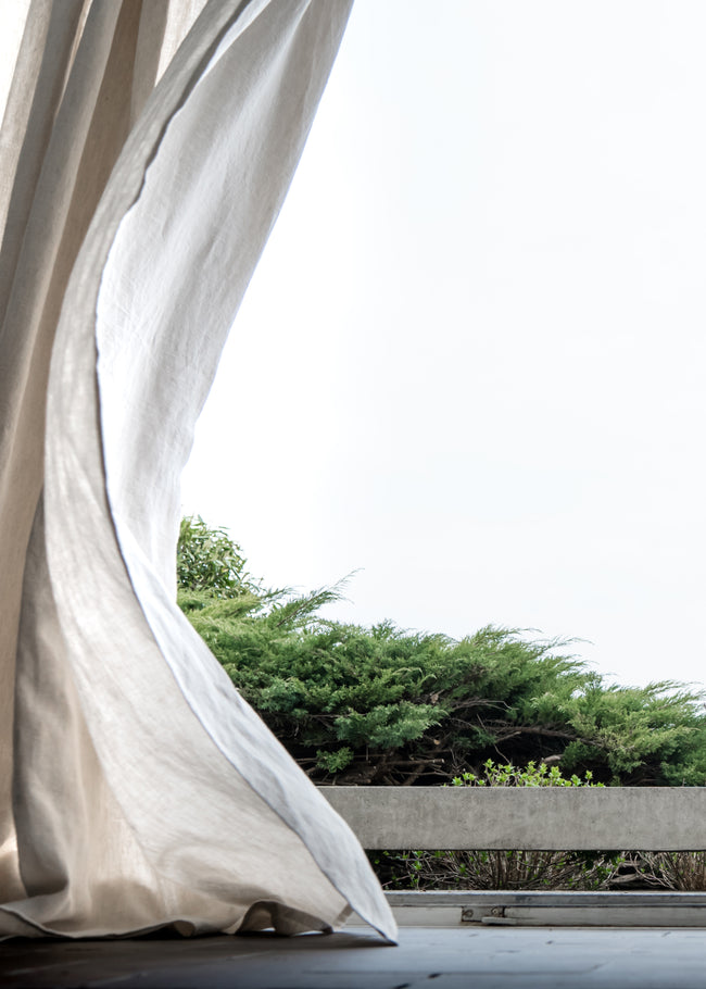 Dynamic breeze oatmeal linen curtain in windy nature setting - Be captivated by the natural elegance of beige linen fabric as it flows gracefully in the wind, surrounded by lush green scenery. Discover the beauty at ann rees.