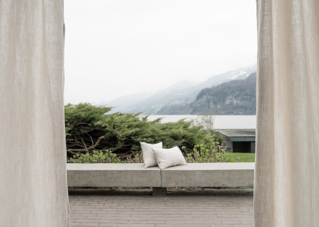 Dynamic breeze oatmeal linen curtain by serene lake - Embrace the natural elegance of beige linen fabric as it gracefully flows in the wind, harmonizing with a picturesque lake view. Discover more at ann rees.